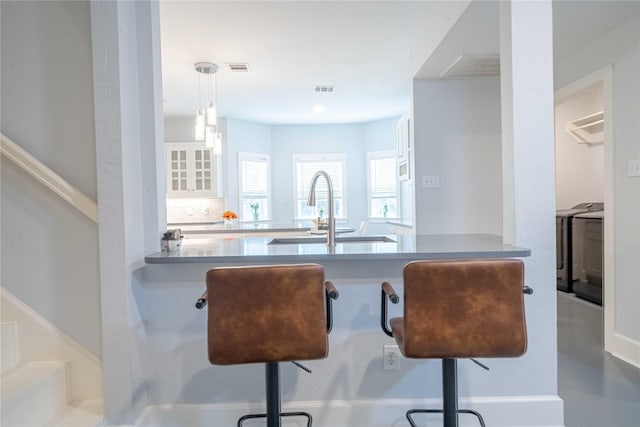 kitchen with a breakfast bar, visible vents, white cabinetry, a sink, and washer / dryer