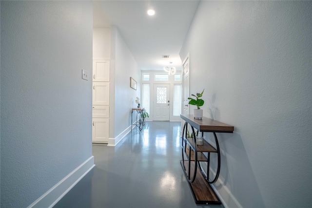 doorway with concrete flooring, visible vents, a textured wall, and baseboards