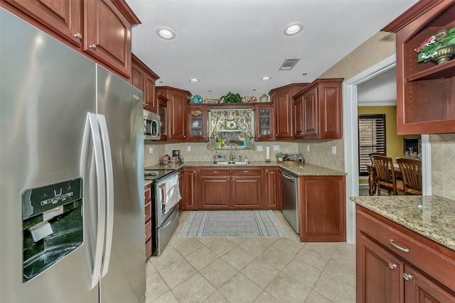 kitchen featuring appliances with stainless steel finishes, tasteful backsplash, sink, light tile patterned floors, and light stone counters