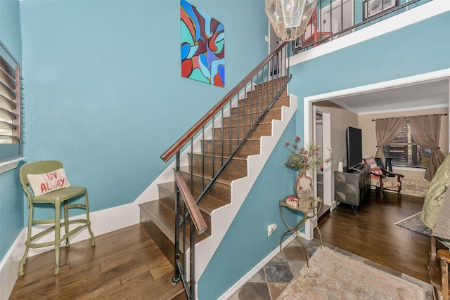 staircase with crown molding, a towering ceiling, and hardwood / wood-style flooring