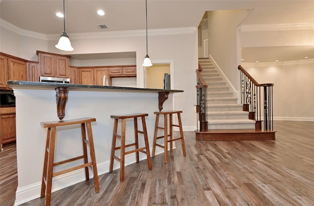 kitchen featuring hanging light fixtures, crown molding, a breakfast bar area, and wood-type flooring