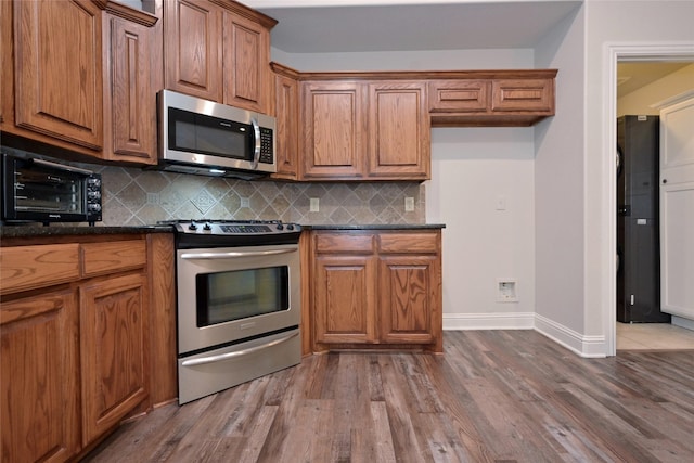 kitchen featuring wood-type flooring, appliances with stainless steel finishes, dark stone counters, and decorative backsplash