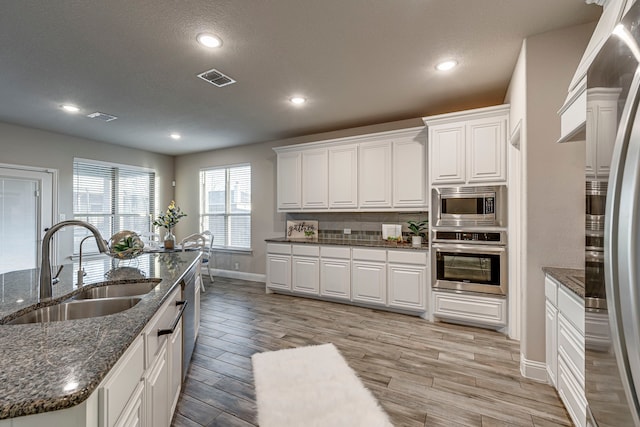 kitchen with appliances with stainless steel finishes, sink, dark stone countertops, and white cabinets