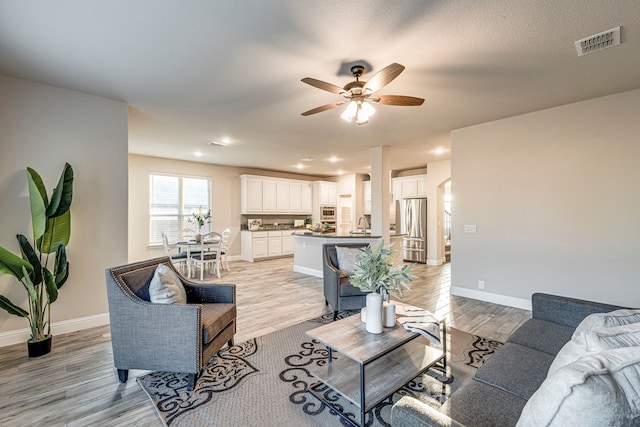 living room with arched walkways, visible vents, light wood-style floors, a ceiling fan, and baseboards