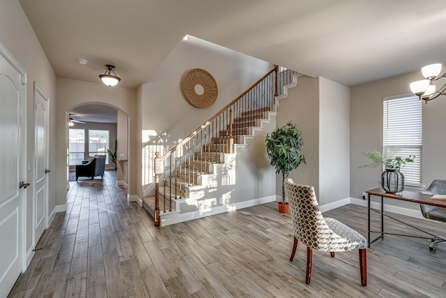 entrance foyer with arched walkways, ceiling fan with notable chandelier, wood finished floors, baseboards, and stairway