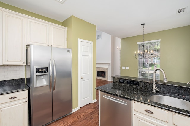 kitchen with dark hardwood / wood-style floors, decorative light fixtures, sink, dark stone counters, and stainless steel appliances