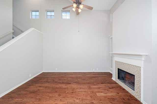 unfurnished living room featuring a high ceiling, a tile fireplace, dark wood-type flooring, and ceiling fan