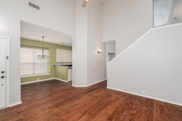 unfurnished living room featuring a towering ceiling, dark hardwood / wood-style flooring, and ceiling fan with notable chandelier