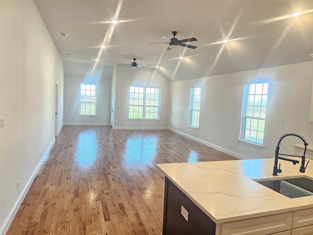 kitchen with lofted ceiling, sink, white cabinetry, light hardwood / wood-style flooring, and light stone countertops