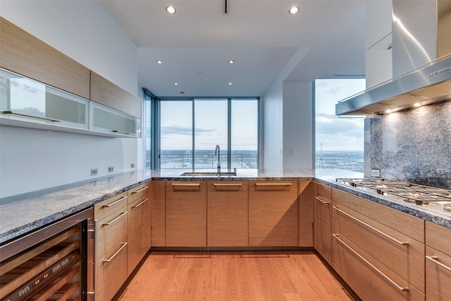 kitchen featuring sink, stainless steel gas cooktop, ventilation hood, beverage cooler, and light hardwood / wood-style floors