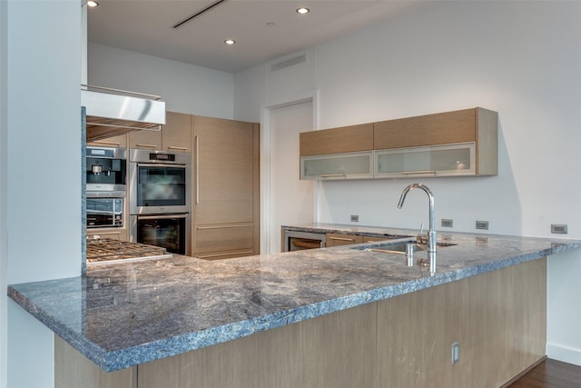 kitchen featuring double oven, dark stone counters, glass insert cabinets, and a sink