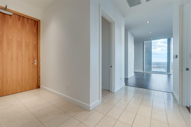 hallway with light tile patterned floors, baseboards, visible vents, recessed lighting, and floor to ceiling windows