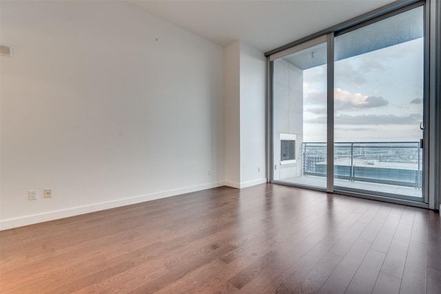 empty room with dark wood finished floors, a wall of windows, and baseboards