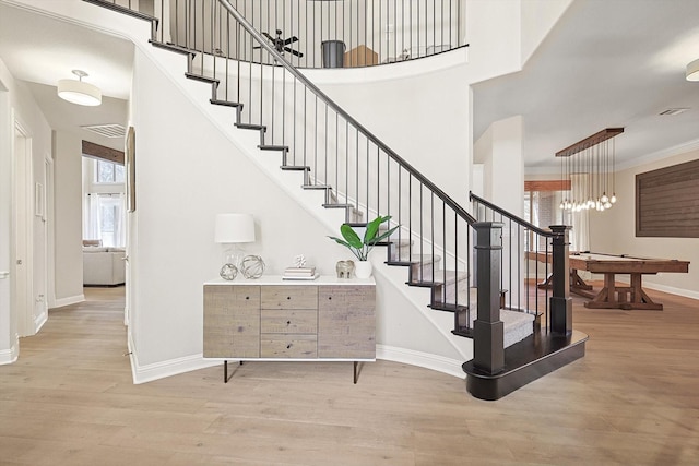 staircase featuring a towering ceiling, ornamental molding, and hardwood / wood-style floors