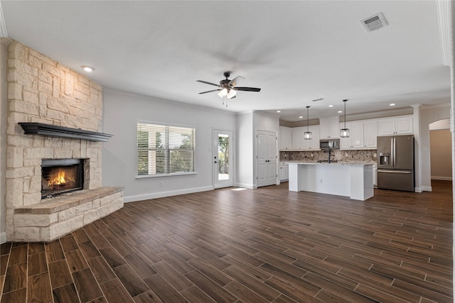 unfurnished living room featuring crown molding, a stone fireplace, and ceiling fan