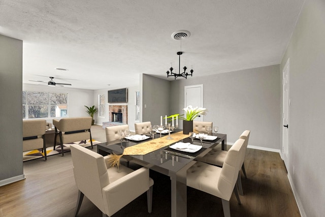 dining area with a brick fireplace, ceiling fan with notable chandelier, hardwood / wood-style floors, and a textured ceiling