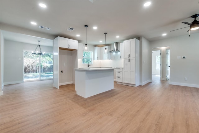 kitchen featuring pendant lighting, white cabinets, a center island, and wall chimney exhaust hood