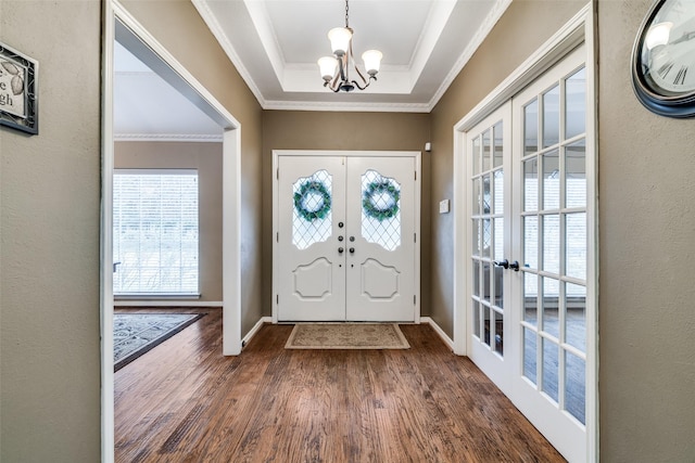 foyer entrance with french doors, dark wood-type flooring, crown molding, a tray ceiling, and a notable chandelier