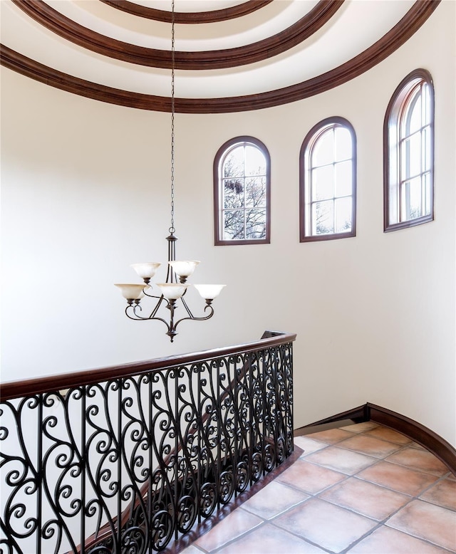 stairs featuring an inviting chandelier, tile patterned flooring, a tray ceiling, and ornamental molding