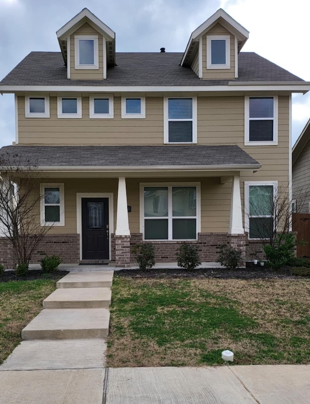 view of front of house featuring a shingled roof, a front yard, a porch, and brick siding