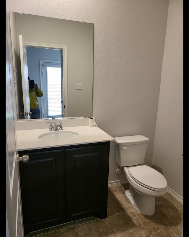 half bathroom with baseboards, vanity, and toilet