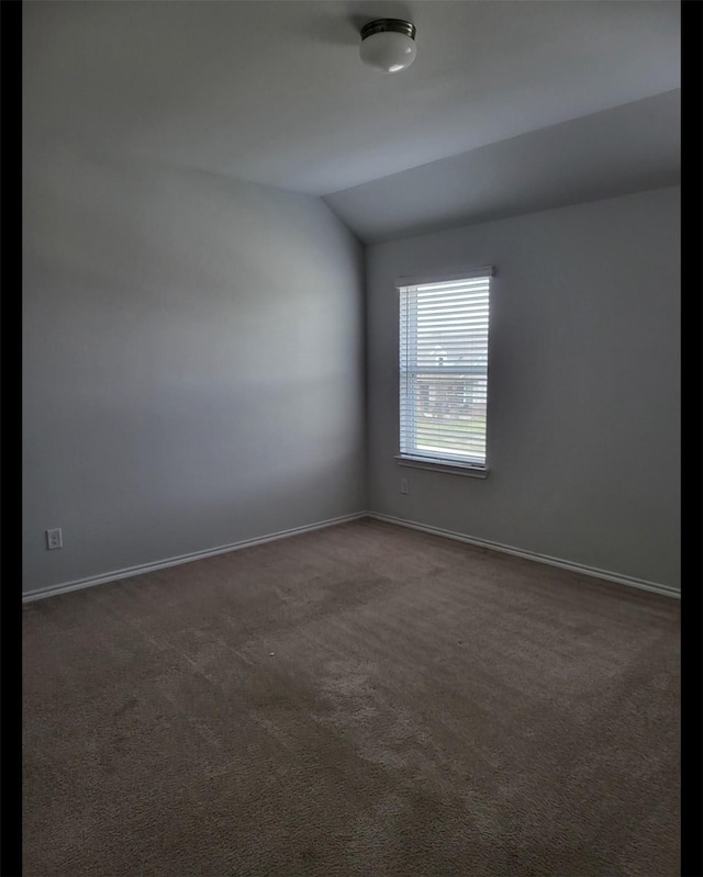 empty room with dark carpet, vaulted ceiling, and baseboards