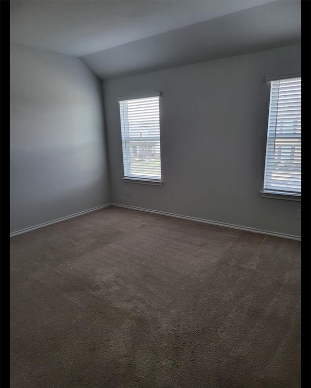 spare room featuring vaulted ceiling, baseboards, and dark colored carpet