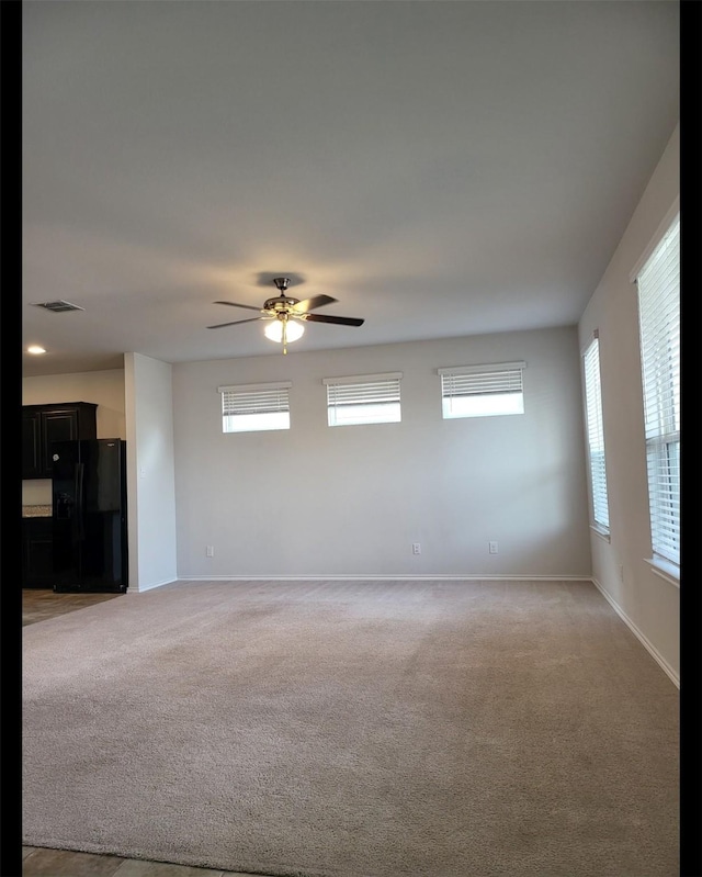 empty room featuring light colored carpet, ceiling fan, visible vents, and baseboards