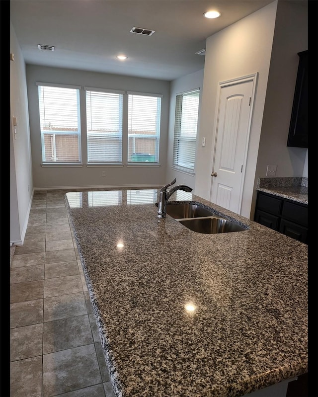 kitchen featuring visible vents, a sink, baseboards, dark stone counters, and a kitchen island with sink