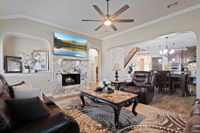 living room featuring hardwood / wood-style flooring, a high end fireplace, ornamental molding, and ceiling fan with notable chandelier