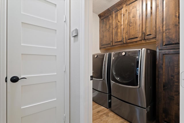 washroom with cabinets, washer and dryer, a textured ceiling, and light hardwood / wood-style floors