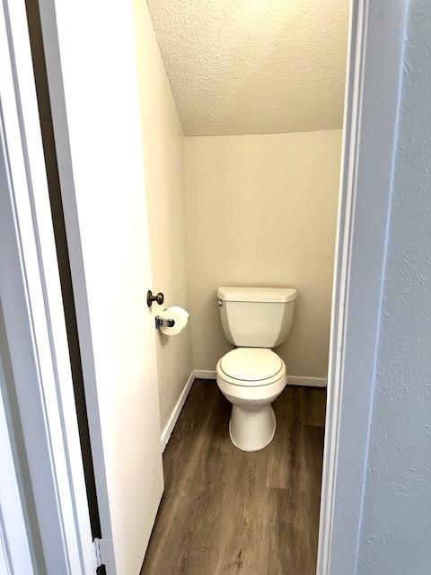 bathroom featuring lofted ceiling, wood-type flooring, toilet, and a textured ceiling