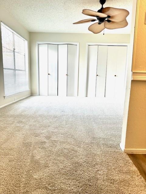 unfurnished bedroom featuring ceiling fan, a textured ceiling, carpet, and two closets