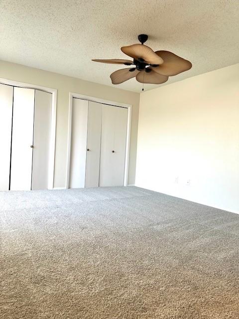 unfurnished bedroom featuring ceiling fan, carpet flooring, two closets, and a textured ceiling