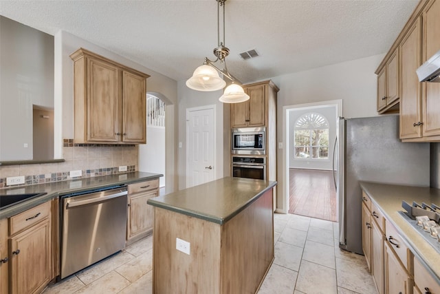 kitchen featuring decorative light fixtures, light tile patterned floors, a kitchen island, stainless steel appliances, and backsplash