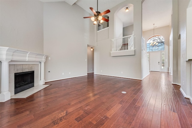 unfurnished living room featuring hardwood / wood-style flooring, a fireplace, high vaulted ceiling, and ceiling fan with notable chandelier