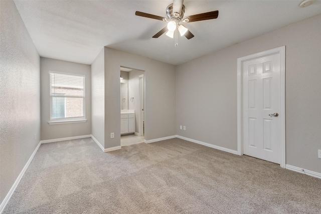 unfurnished bedroom featuring ceiling fan, light colored carpet, and ensuite bath