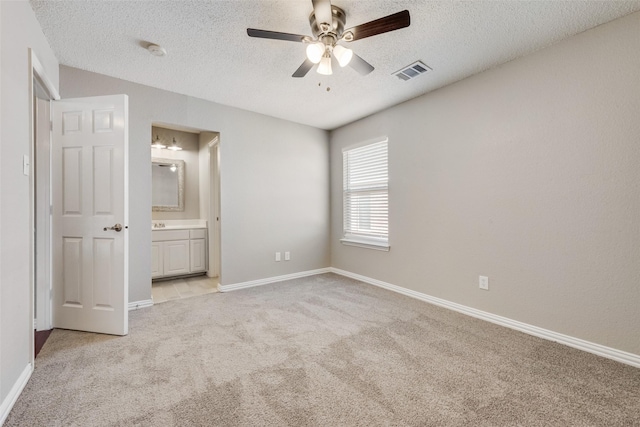 unfurnished bedroom featuring light carpet, ceiling fan, a textured ceiling, and ensuite bathroom