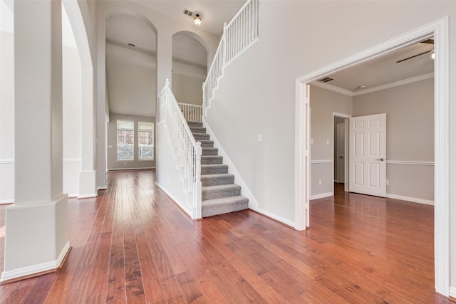 entryway with decorative columns, crown molding, a towering ceiling, and hardwood / wood-style floors