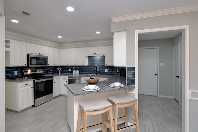 kitchen featuring a breakfast bar area, stainless steel appliances, kitchen peninsula, and white cabinets