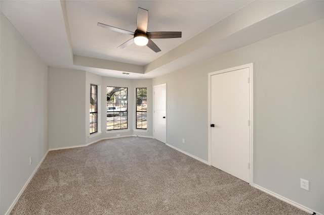 unfurnished room with a raised ceiling, carpet, and ceiling fan