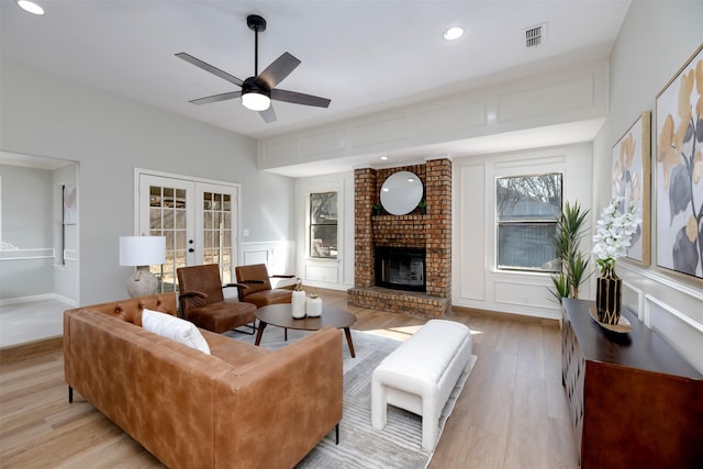 living room featuring ceiling fan, a brick fireplace, light hardwood / wood-style floors, and french doors