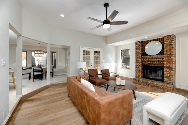 living room featuring ceiling fan with notable chandelier, a fireplace, french doors, and light wood-type flooring