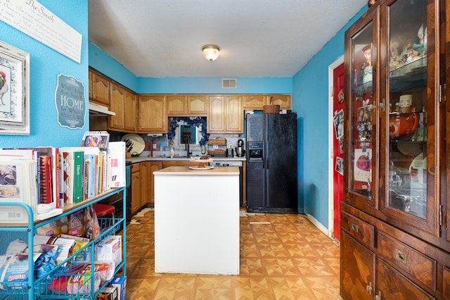 kitchen with visible vents, baseboards, light countertops, black fridge, and brown cabinetry