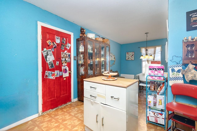 kitchen with a notable chandelier, light countertops, hanging light fixtures, white cabinets, and baseboards