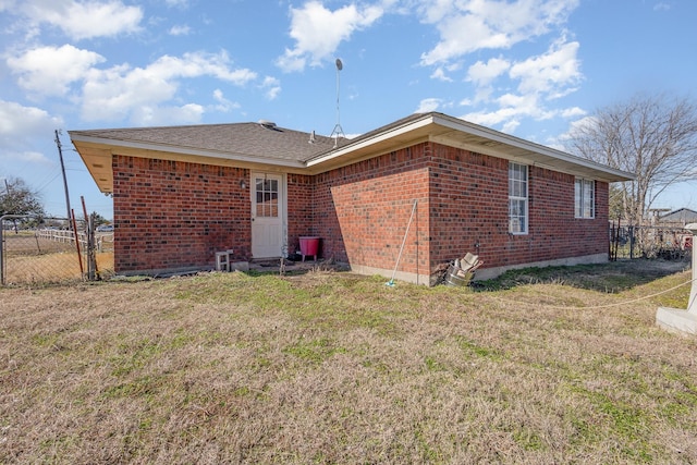 rear view of house featuring brick siding, fence, and a lawn