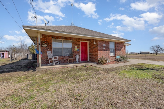 view of front of home featuring a shingled roof, covered porch, fence, a front lawn, and brick siding