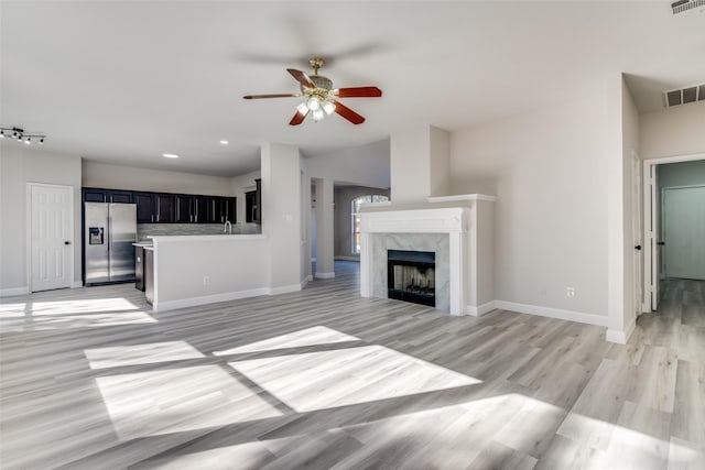 unfurnished living room with a premium fireplace, sink, ceiling fan, and light hardwood / wood-style flooring