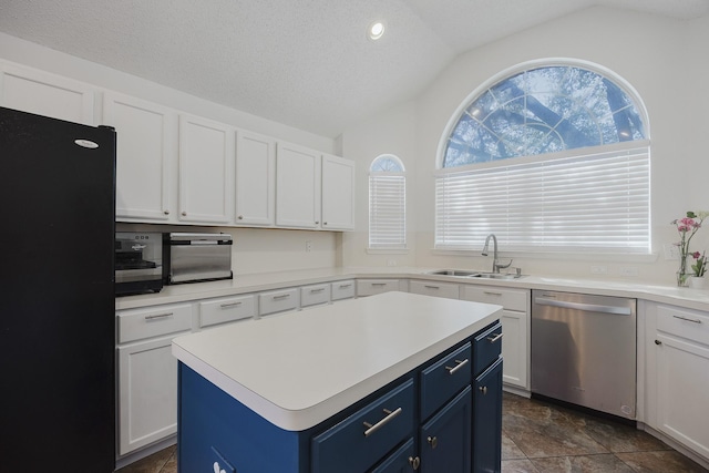 kitchen with a sink, vaulted ceiling, stainless steel dishwasher, blue cabinetry, and freestanding refrigerator