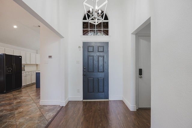 foyer with an inviting chandelier, a high ceiling, baseboards, and dark wood-type flooring